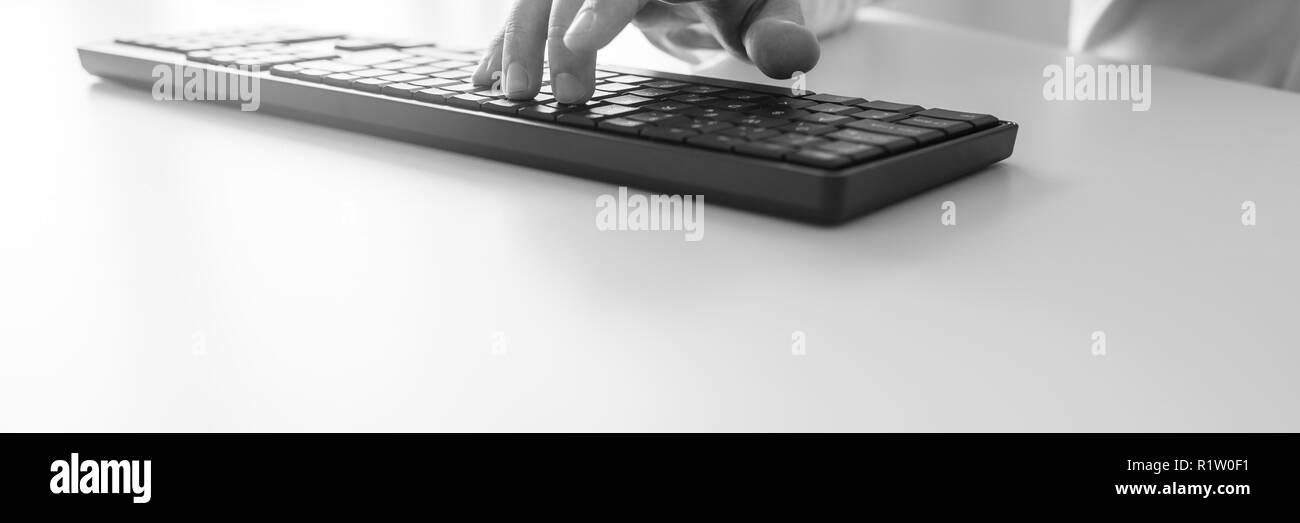 In der breiten Ansicht schwarz-weiss Bild des Geschäftsmannes hand Tippen auf Black Office Computer Tastatur auf weißem Schreibtisch. Stockfoto