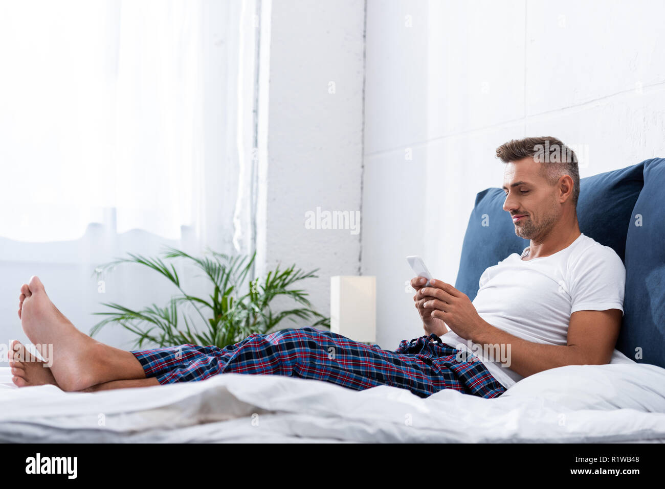 Erwachsenen Mann im weißen T-Shirt mit Smartphone während der Zeit im Bett zu Hause. Stockfoto