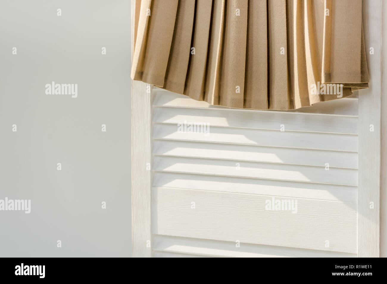 Nahaufnahme der beige Faltenrock an den weißen Raumteiler isoliert auf Grau Stockfoto
