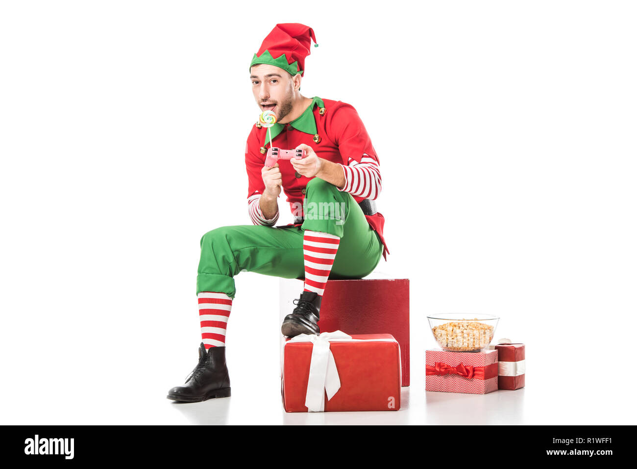 Mann in der Weihnachtself kostüm sitzen auf Haufen präsentiert mit Lollipop  und spielen video game isoliert auf weißem Stockfotografie - Alamy