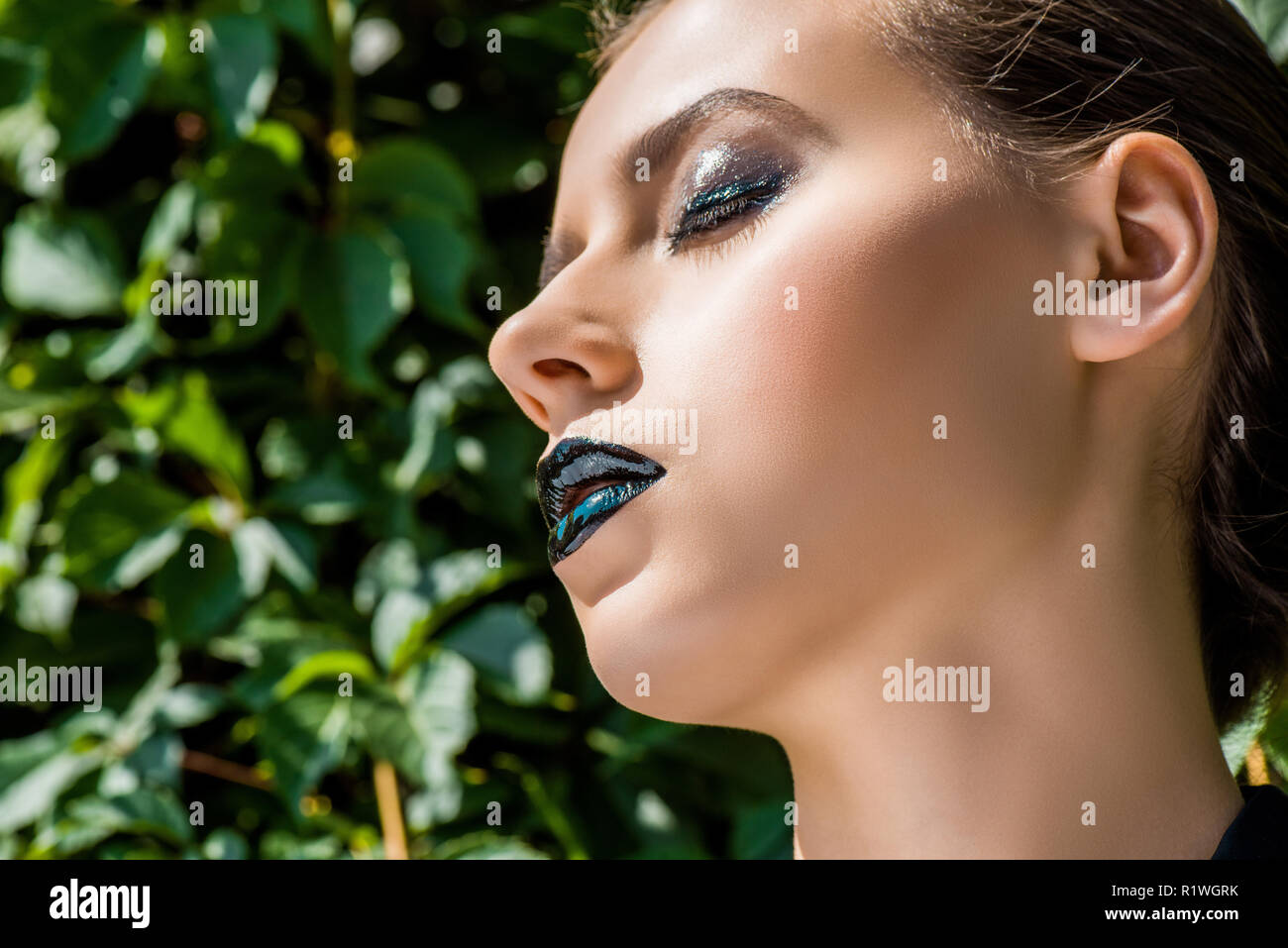 Junge Frau mit schwarzen Lippen und grüne Blätter im Hintergrund Stockfoto