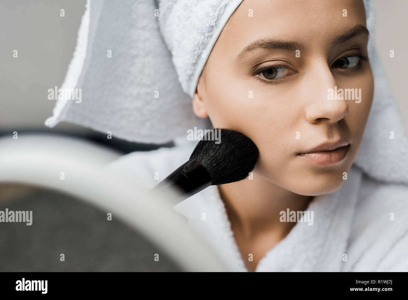 Schöne Mädchen in ein Handtuch auf dem Kopf Anwendung Pulver mit kosmetischen Bürste und Spiegel Stockfoto