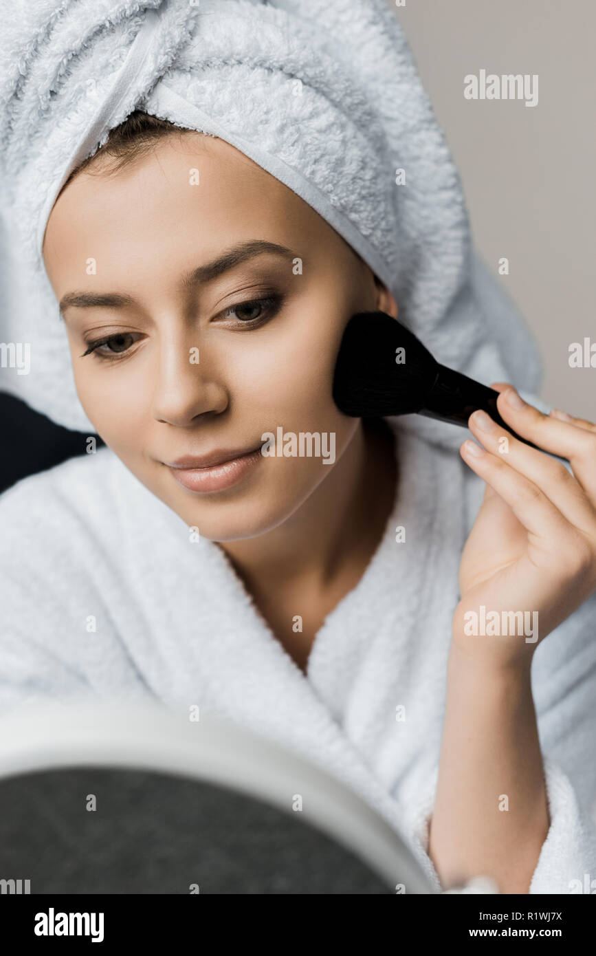 Lächelnde Frau in Bademantel und Badetuch Anwendung Pulver mit kosmetischen Bürste Stockfoto