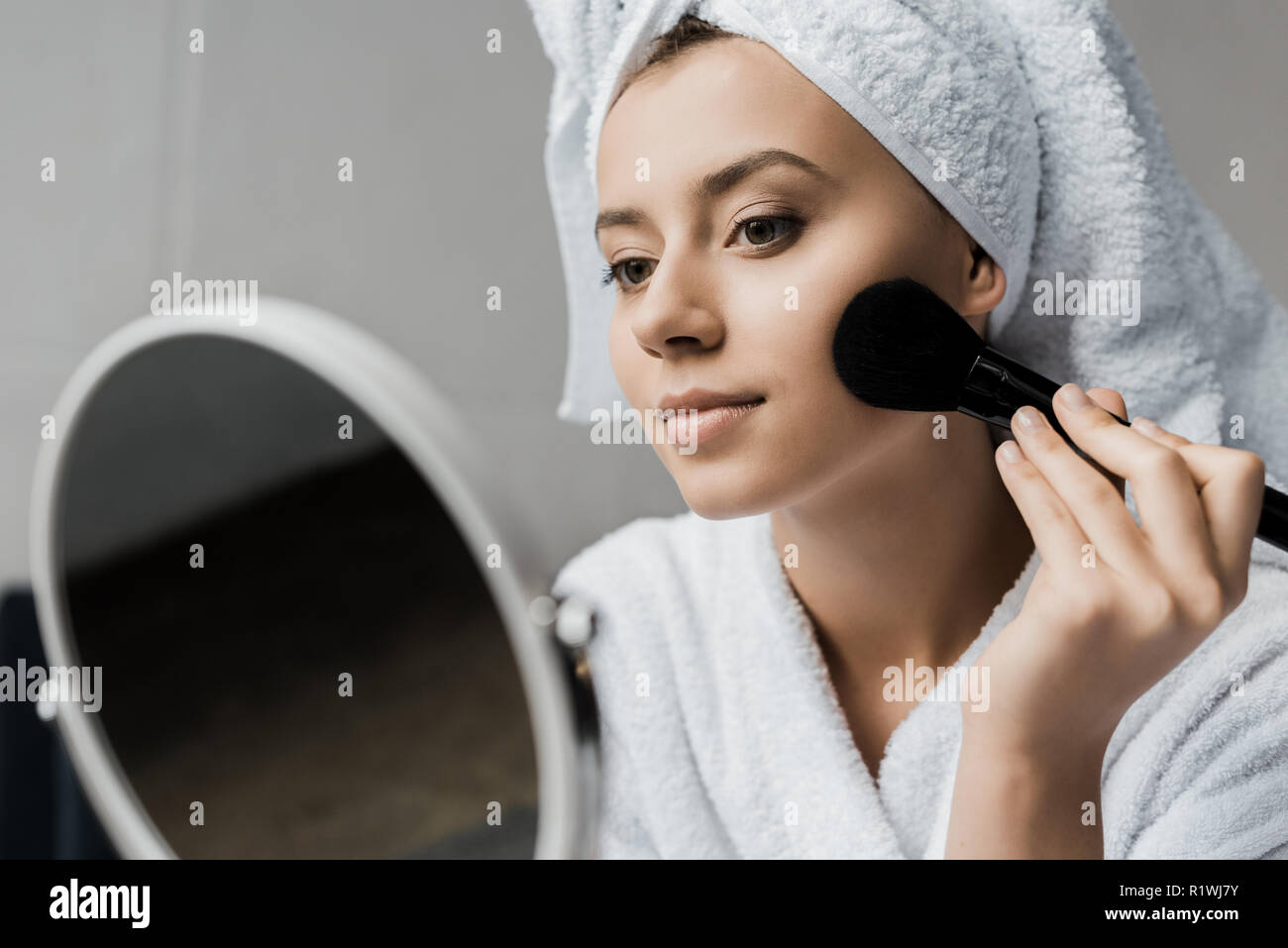 Attraktives Mädchen Anwendung Pulver mit kosmetischen Bürste und Spiegel Stockfoto
