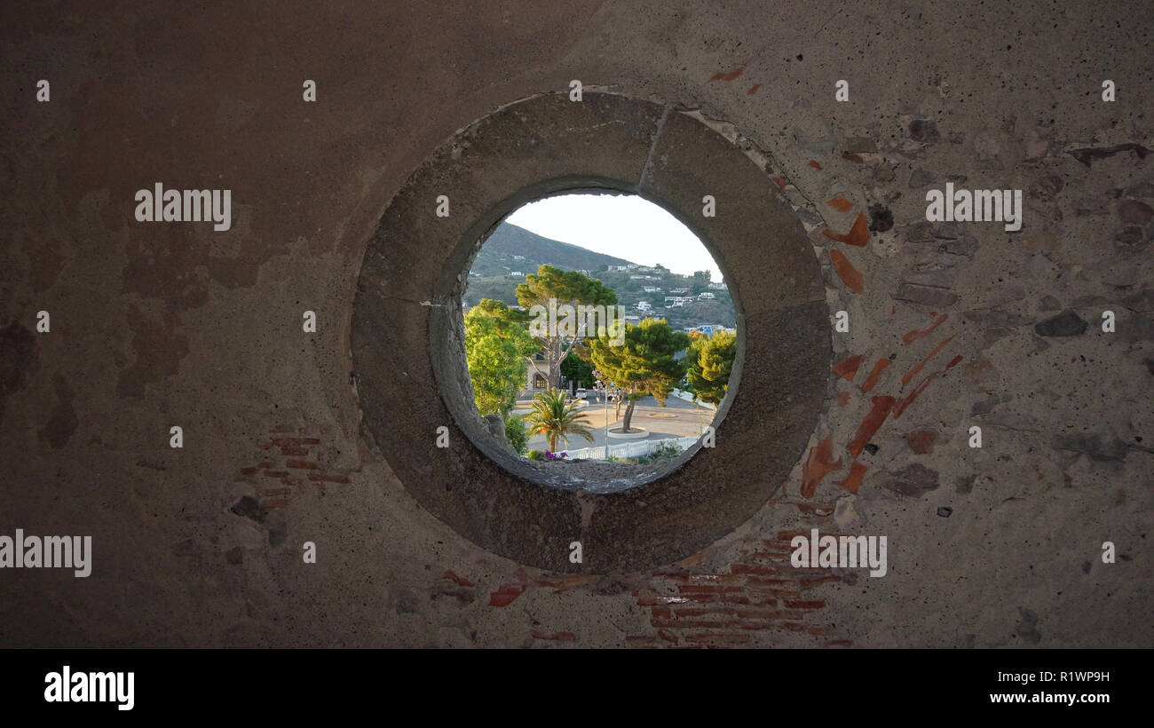 Blick durch ein rundes Fenster in einer Steinmauer zum Dorf Lipari in Italien Stockfoto