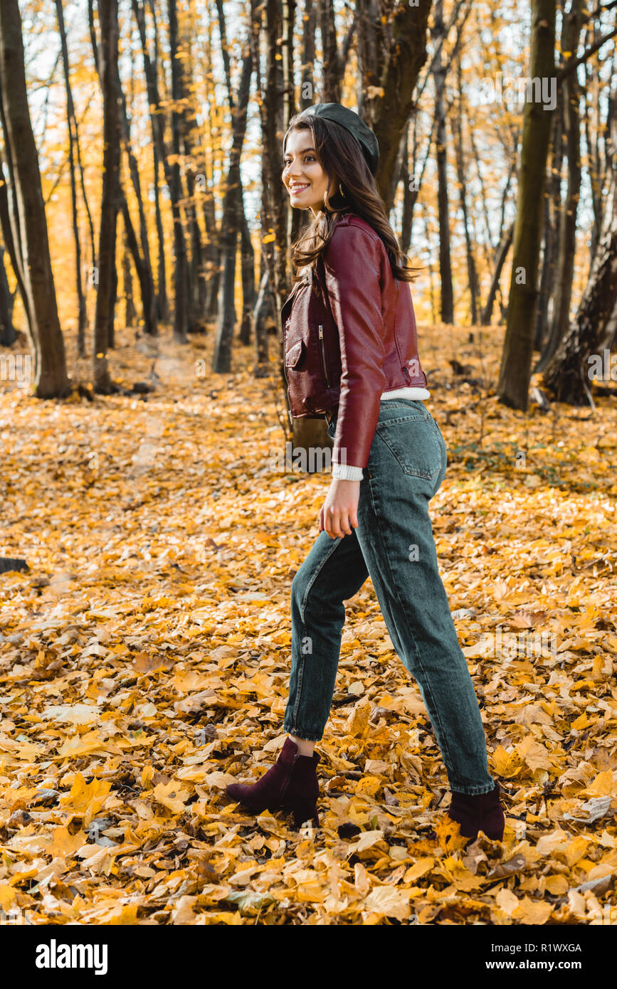 Attraktive stilvolle Frau in Baskenmütze und Lederjacke wandern in herbstlichen Park Stockfoto