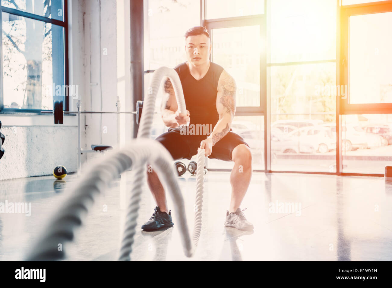 Junge Sportler, die mit der Schlacht Seile im Fitnessstudio im Sonnenlicht Stockfoto