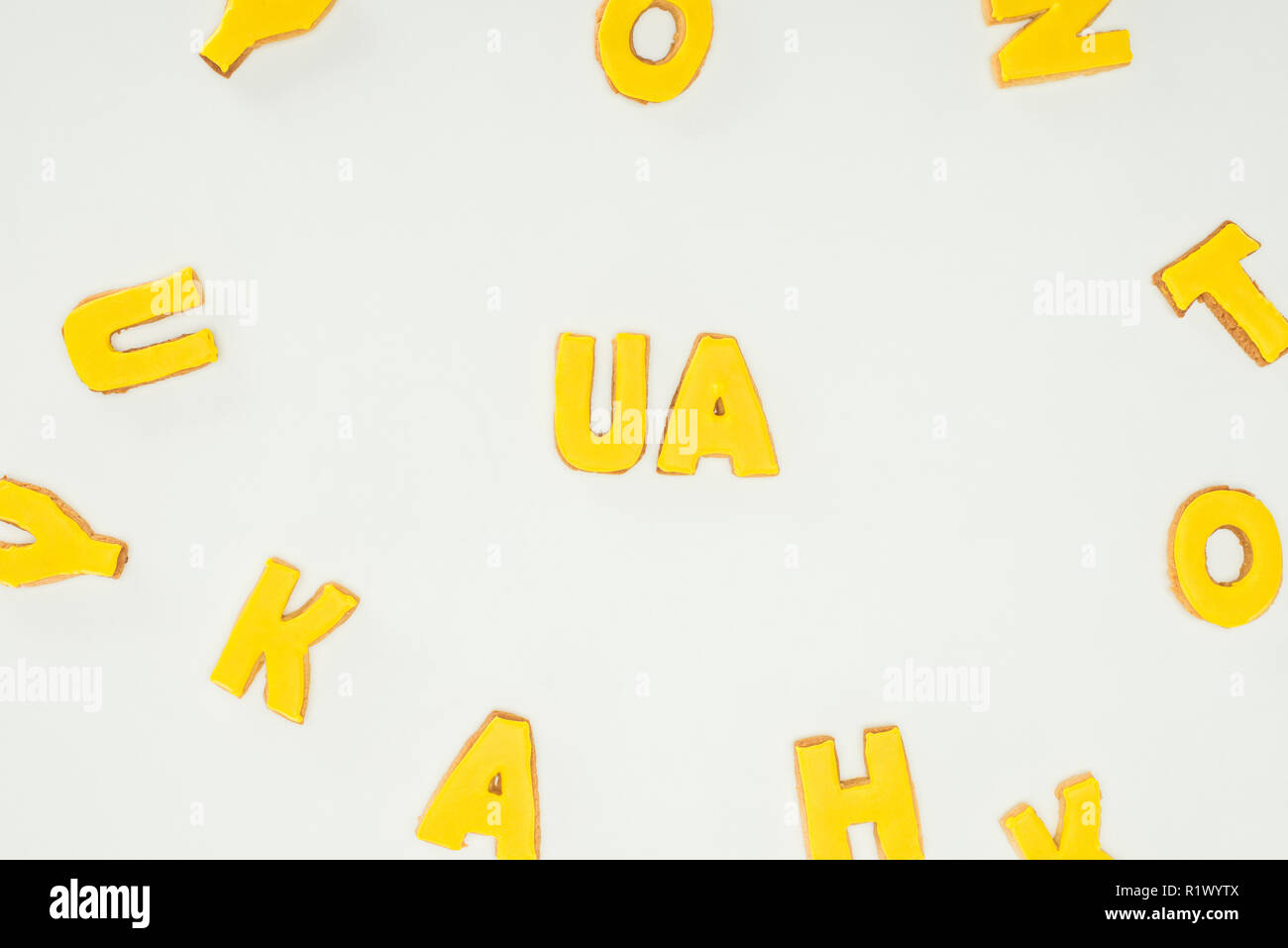 Ua Zeichen aus gelben Cookies und zerstreut Alphabet Buchstaben auf weißem Hintergrund Stockfoto