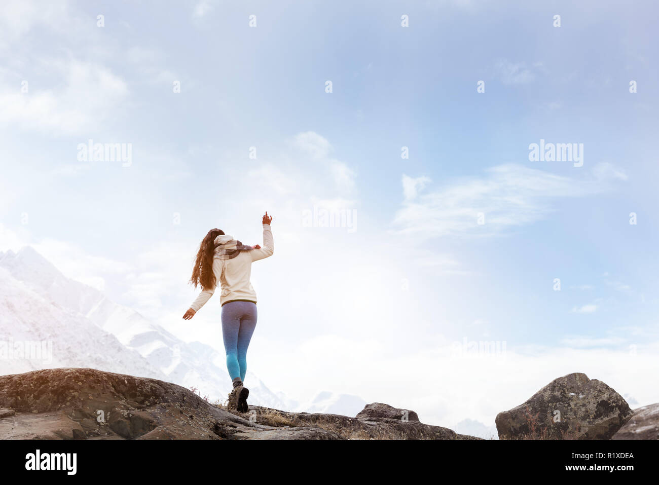 Dame ist zu Fuß durch große Felsen auf dem Hintergrund der schneebedeckten Berge Stockfoto
