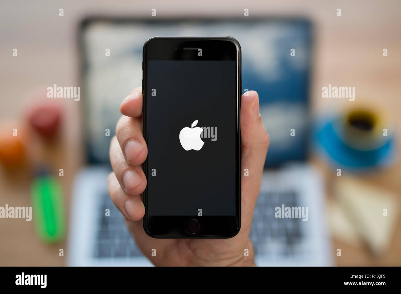 Ein Mann schaut auf seinem iPhone das Apple Logo, während saß an seinem Computer Schreibtisch (nur redaktionelle Nutzung). Stockfoto