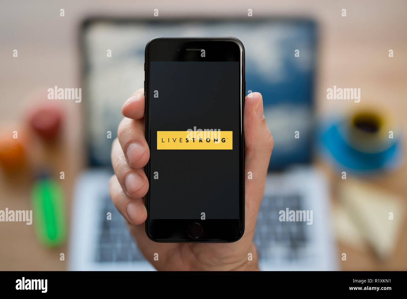 Ein Mann schaut auf seinem iPhone. Das Leben starke Logo, während saß an seinem Computer Schreibtisch (nur redaktionelle Nutzung). Stockfoto