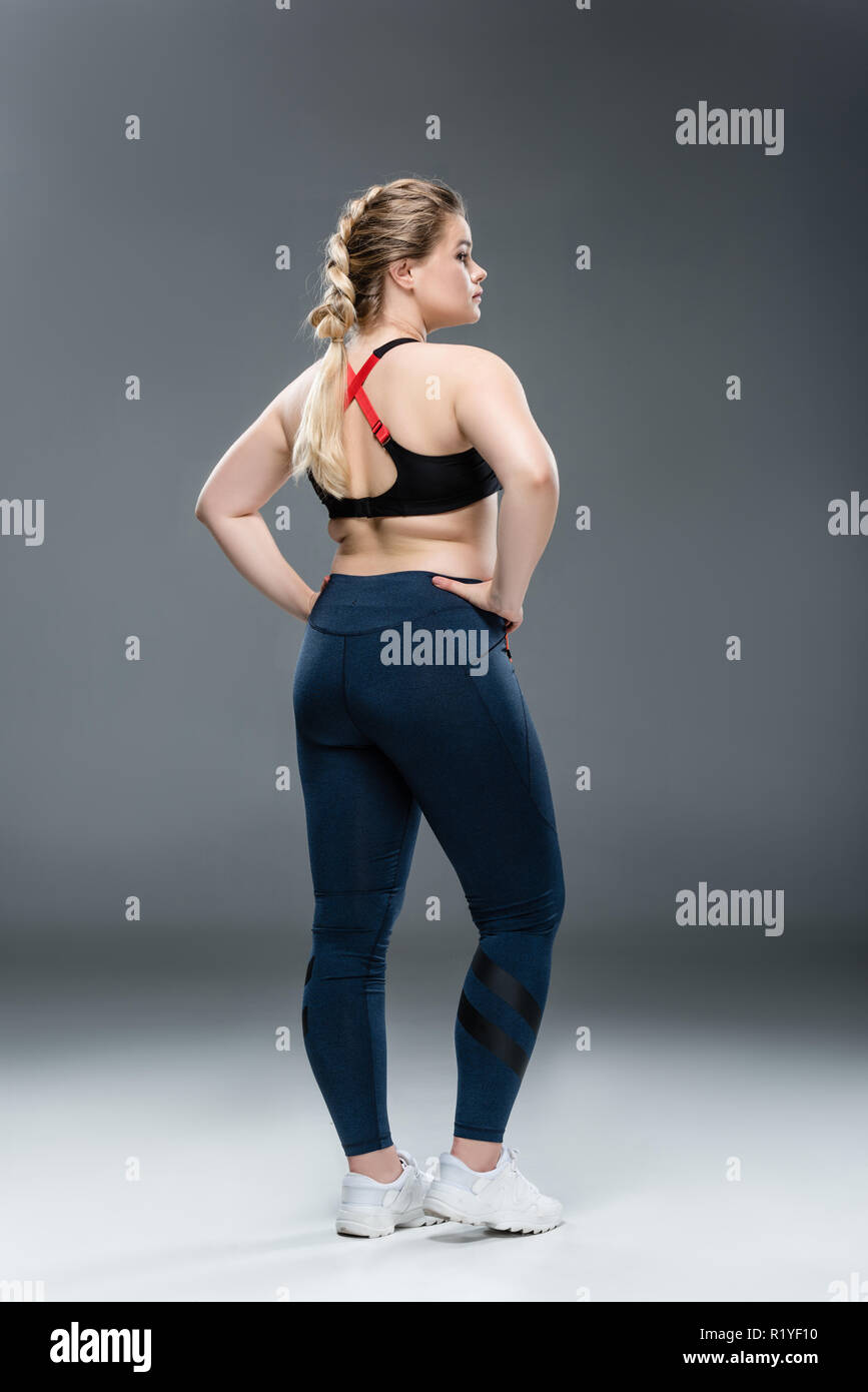 Zurück Blick auf junge übergewichtige Frau in Sportkleidung auf Taille auf Grau Stockfoto