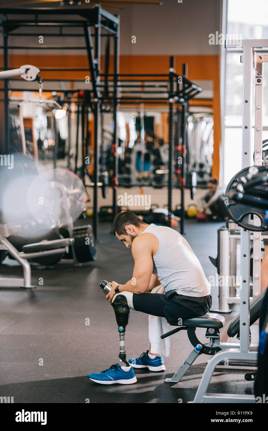 Müde junge Sportler mit künstlichen Bein sitzen im Fitnessraum Stockfoto