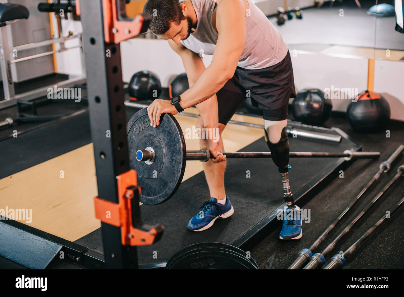 Hübscher junger Sportler mit künstlichen Bein Gewichtszunahme die Platte an der Bar im Fitnessstudio vor dem Training Stockfoto
