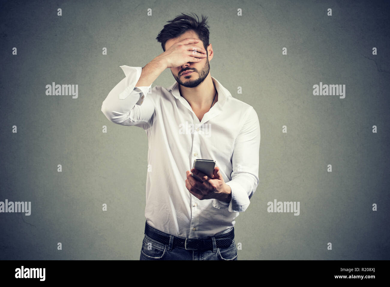 Legerer Mann für Gesicht in Verzweiflung mit schlechten Nachrichten auf dem Smartphone gegen grauer Hintergrund Stockfoto