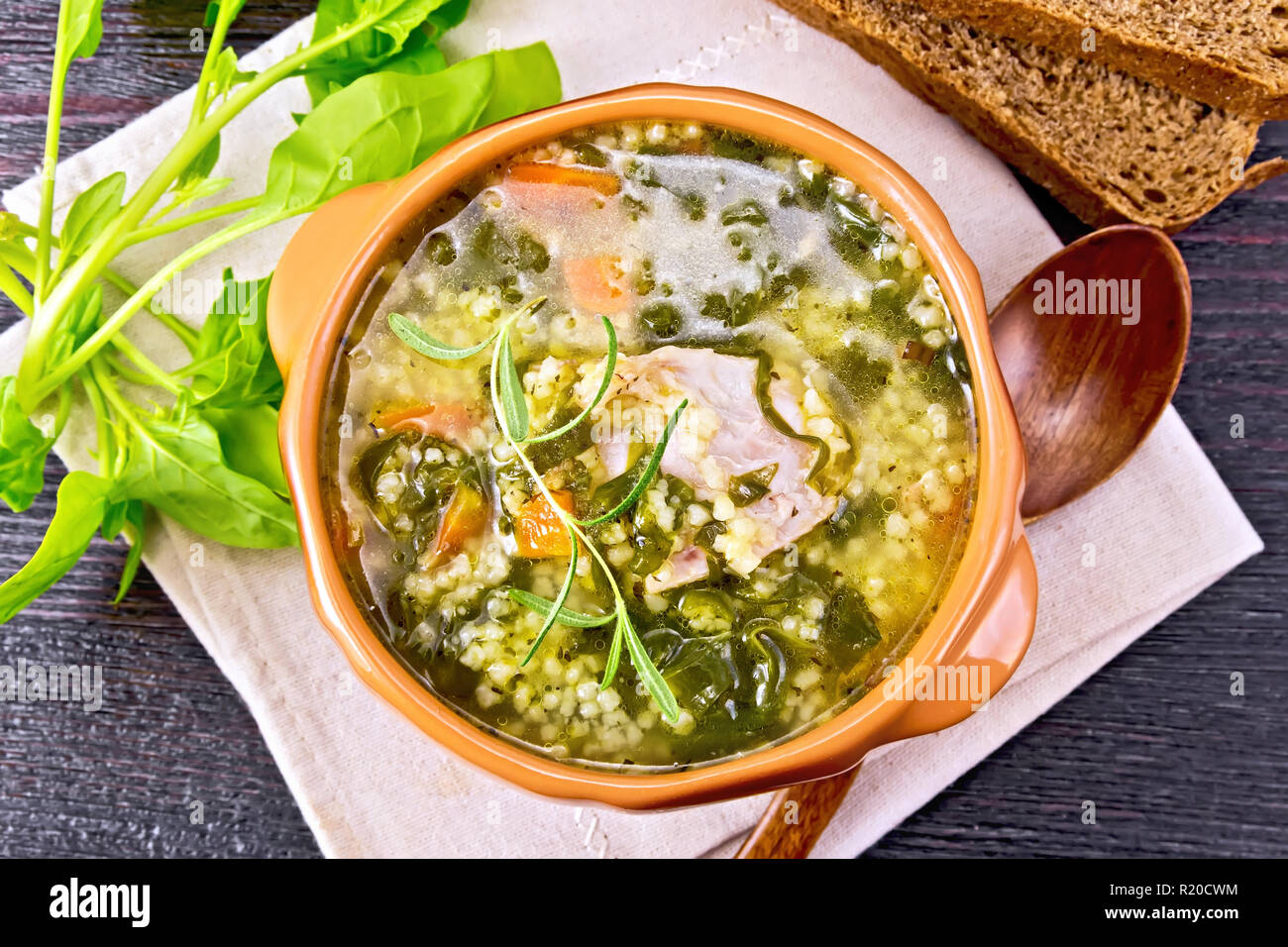 Schweinerippchen Suppe mit Couscous und Spinat in einer Schüssel auf Serviette, Brot auf Holzbrett Hintergrund von oben Stockfoto