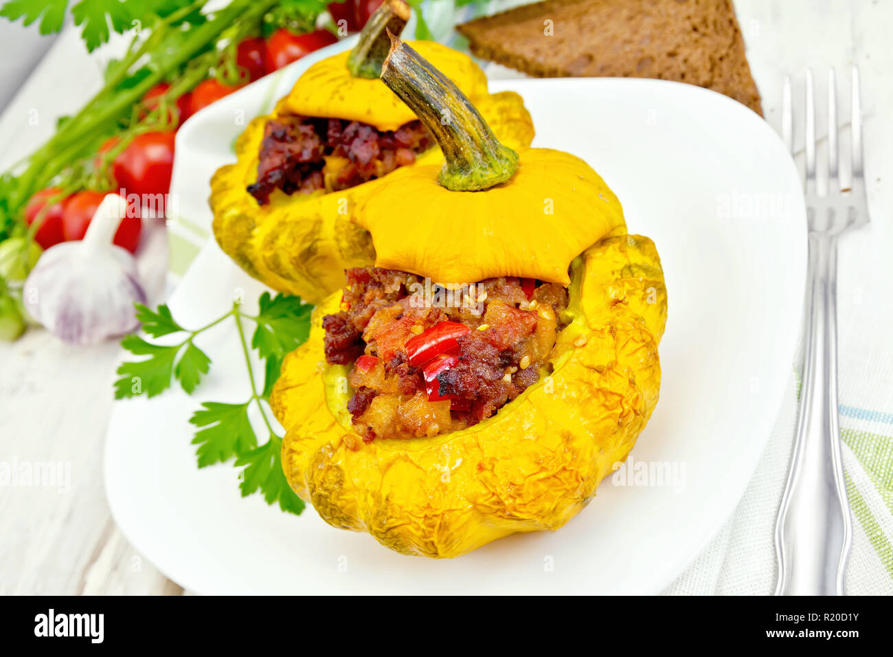 Zwei gelbe Zucchini gefüllt mit Fleisch, Tomaten und Paprika in die Schüssel, Brot, Knoblauch, Petersilie und eine Serviette auf dem Hintergrund Licht Holzbretter Stockfoto