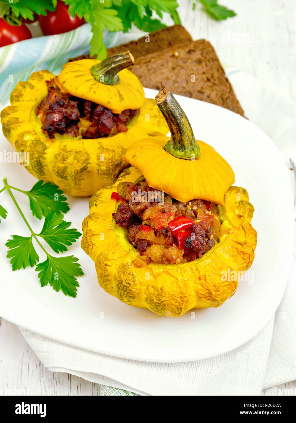 Zwei gelbe Zucchini gefüllt mit Fleisch, Tomaten und Paprika in die Schüssel, Brot, Petersilie und eine Serviette auf dem Hintergrund Licht Holzbretter Stockfoto