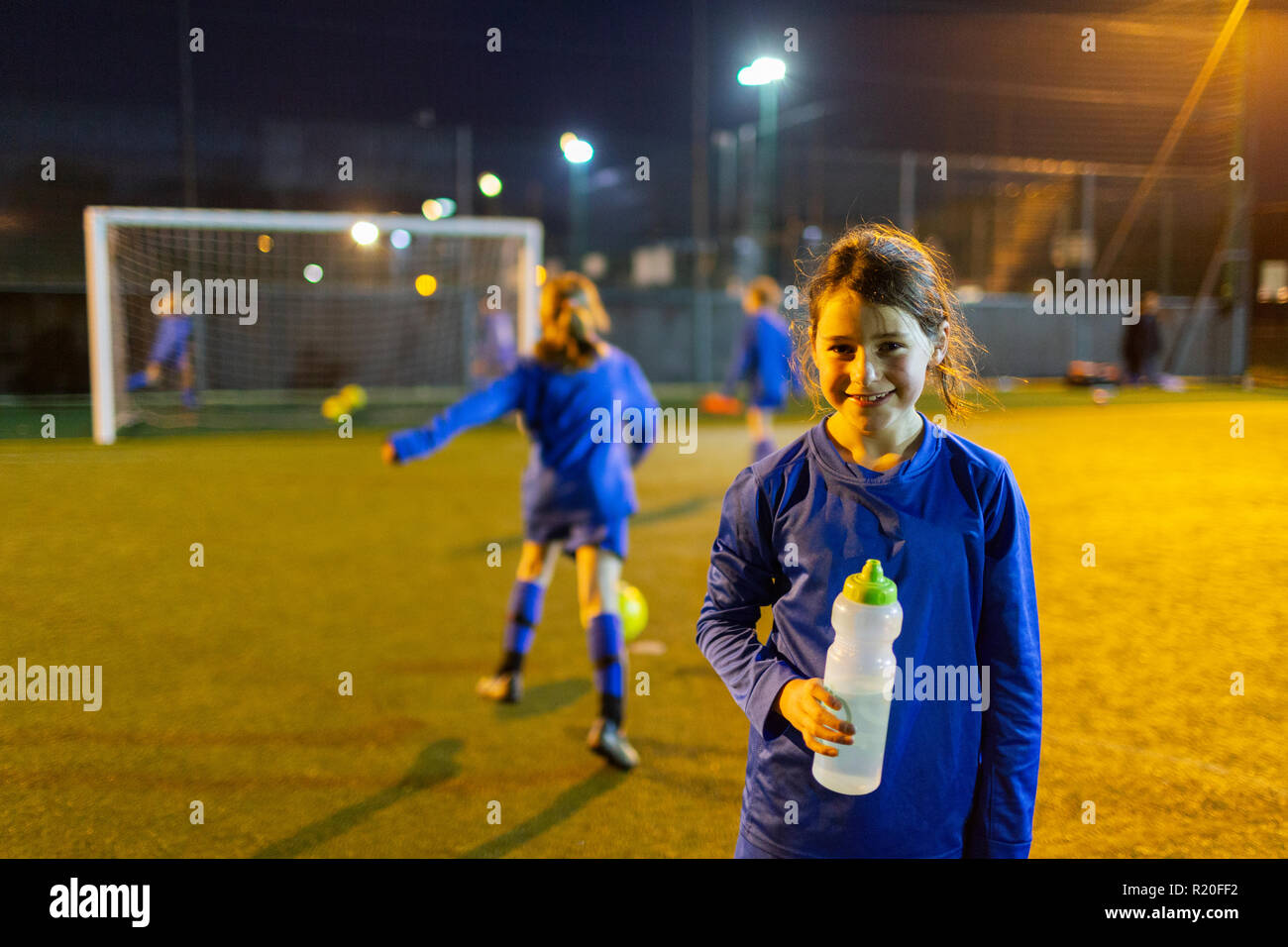 Portrait lächelnde Mädchen Fußball-Spieler Trinkwasser auf dem Feld in der Nacht Stockfoto