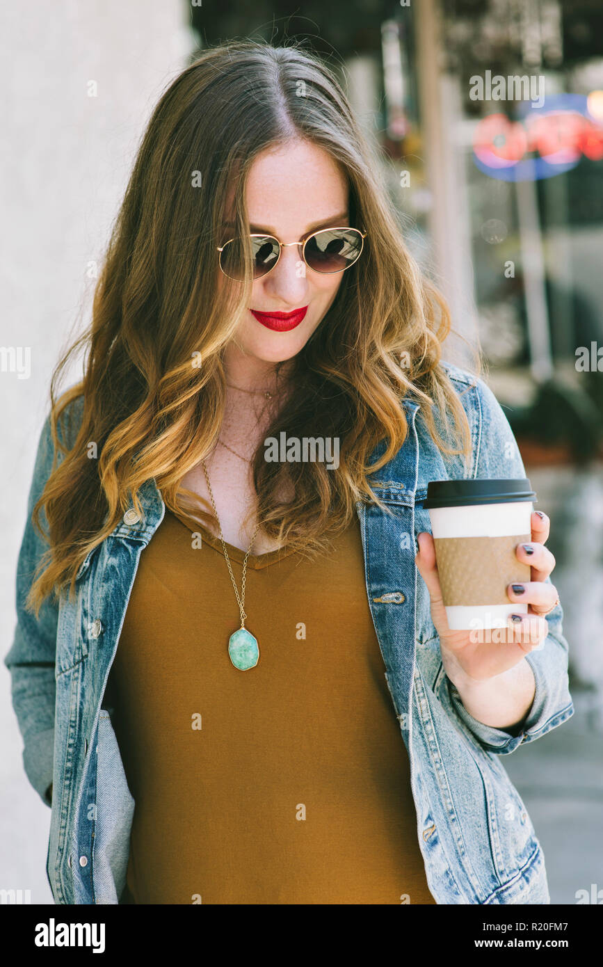 Eine Frau mit Sonnenbrille auf steht, während Sie eine Tasse Kaffee Stockfoto