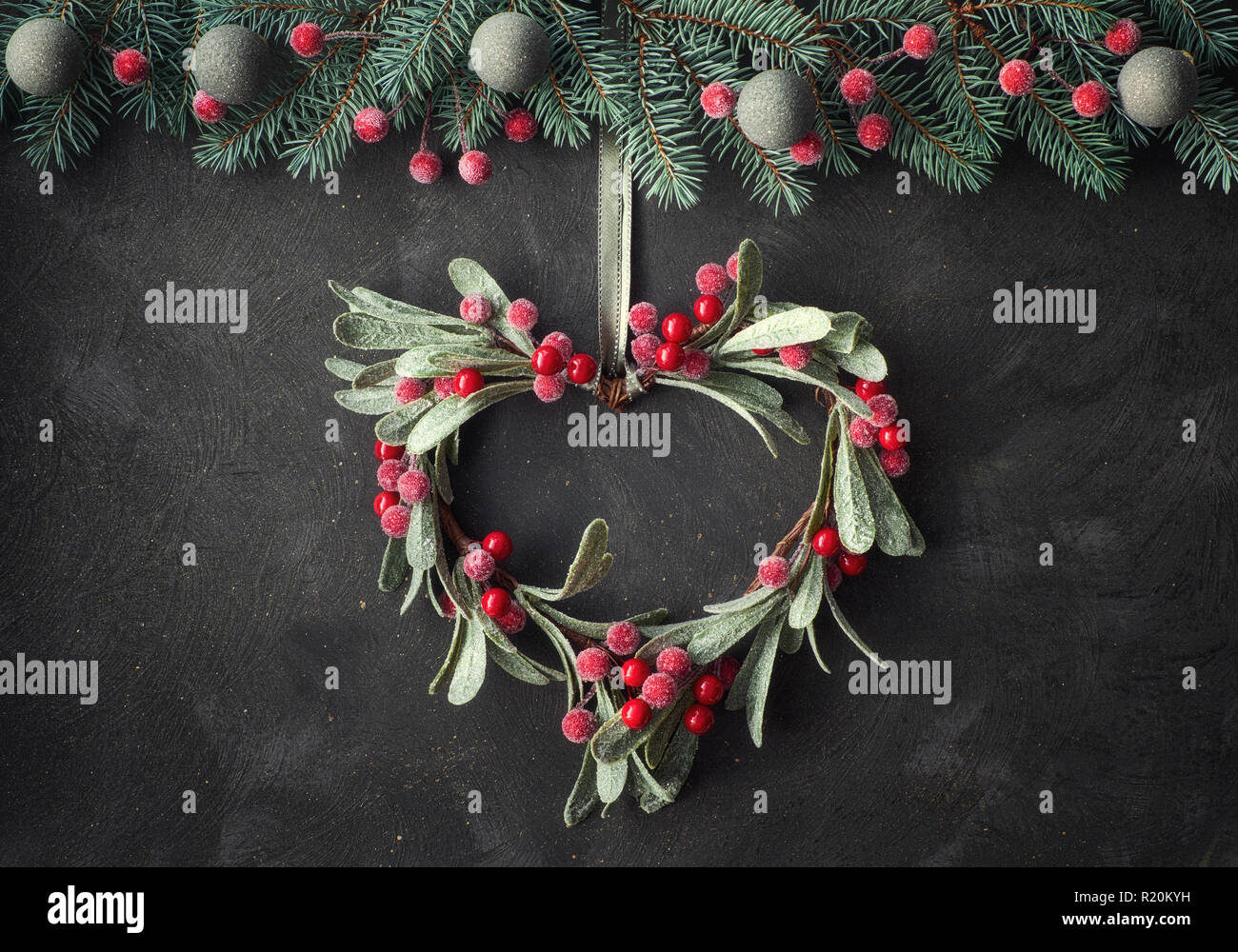 Heart-shaped Mistel Weihnachten Kranz und festliche Girlande aus tanne Zweige, frosted Beeren und Schmuckstücke, auf dunklem Hintergrund Stockfoto