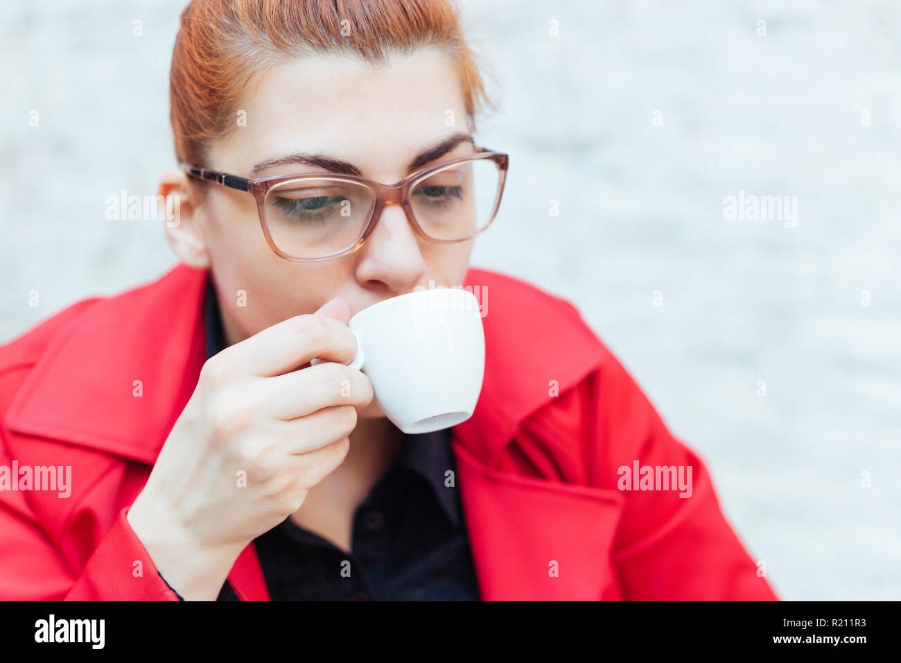 redhead grild in einem roten mantel trinken einen espresso stockfoto