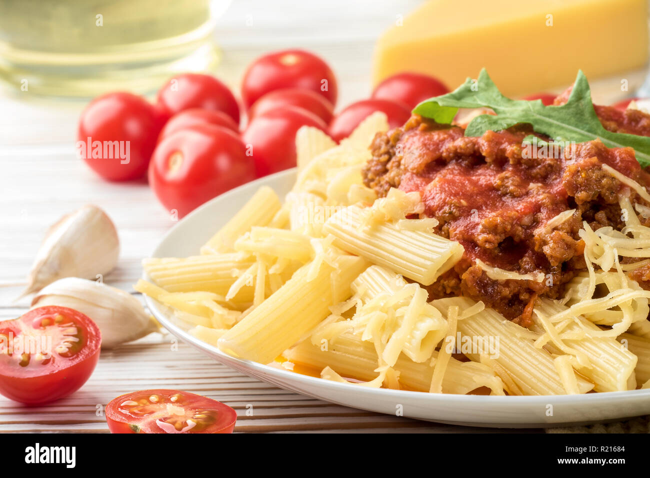 Italienische Pasta Bolognese Penne rigatone Hackfleisch in Tomatensoße und Parmesan. Noch immer leben auf weiße Holztisch mit Cherry Tomaten serviert, Karaffe Olivenöl und Glas Weißwein Stockfoto