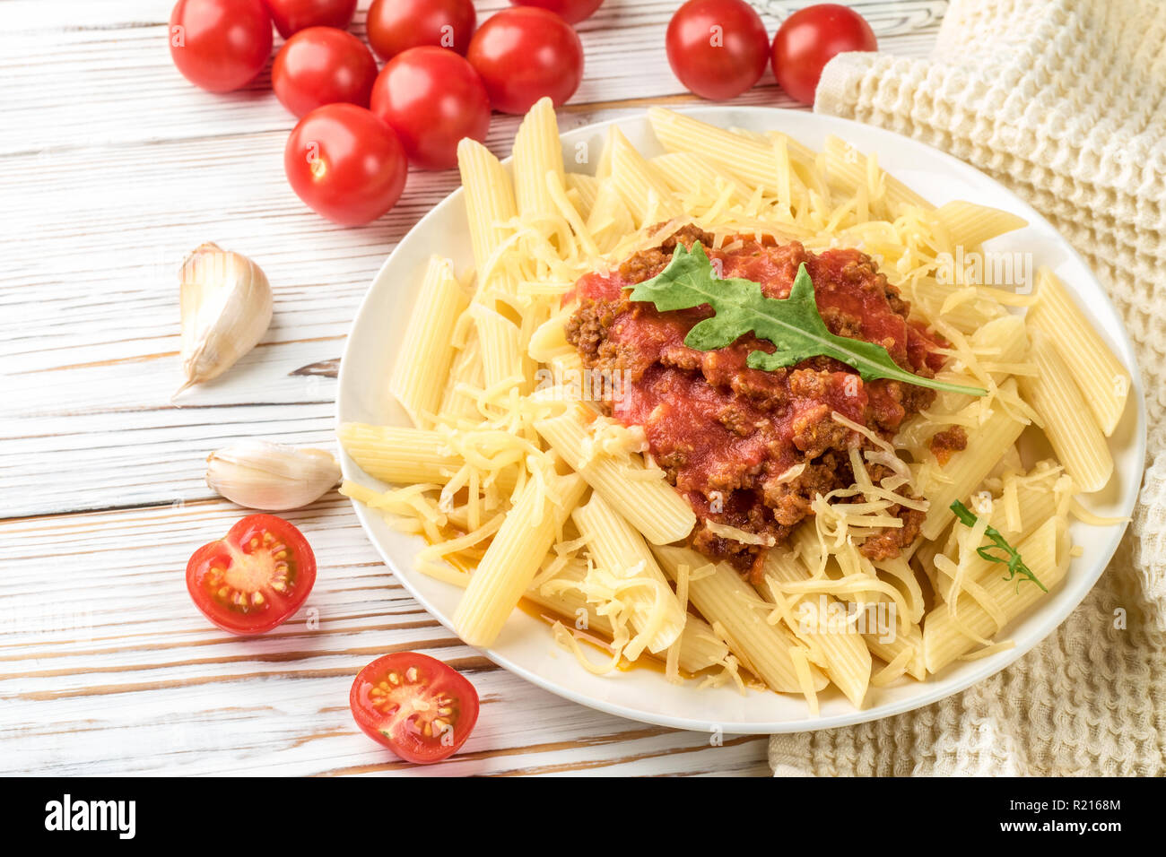 Italienische Pasta Bolognese Penne rigatone Hackfleisch in Tomatensoße und Parmesan. Noch immer leben auf weiße Holztisch mit Cherry Tomaten serviert, Karaffe Olivenöl und Glas Weißwein Stockfoto
