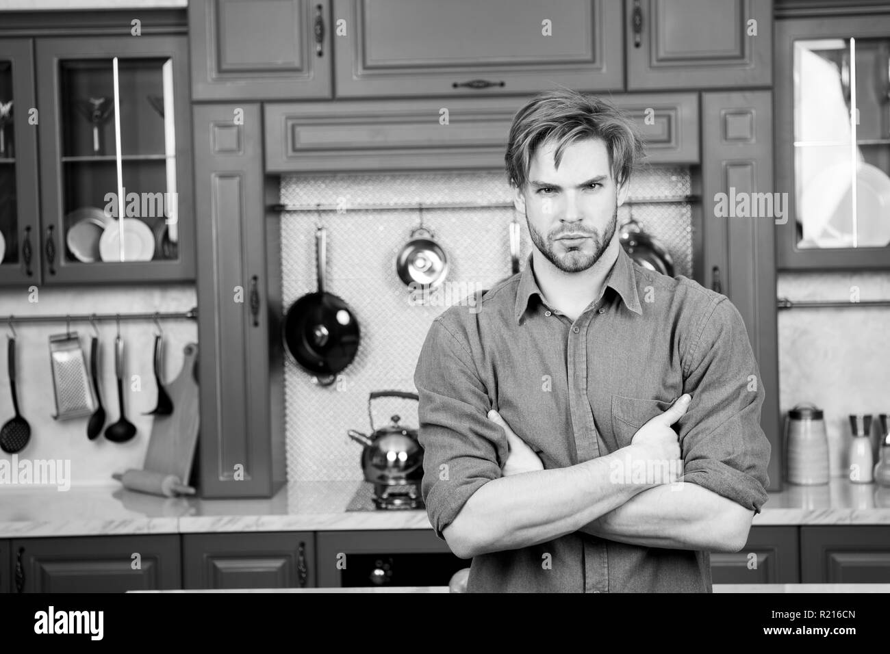 Macho mit ernsten Gesicht, blonde Haare, blaue T-Shirt stand mit gefalteten Händen in der Küche. Zubereitung von Speisen, Küche, Kochen Konzept. Stockfoto
