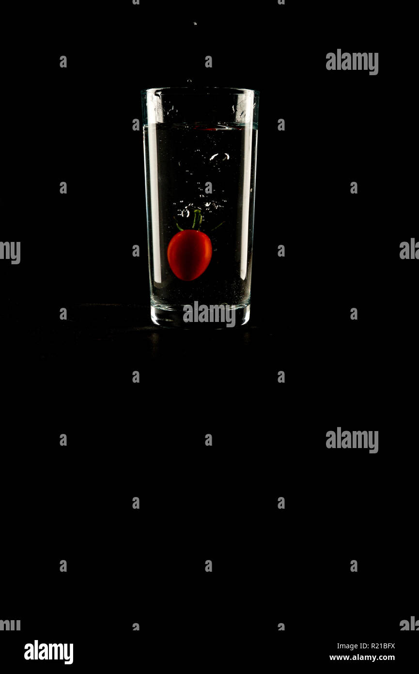 Ein Baby tomato planschen in einem Glas Wasser auf schwarzem Hintergrund Stockfoto