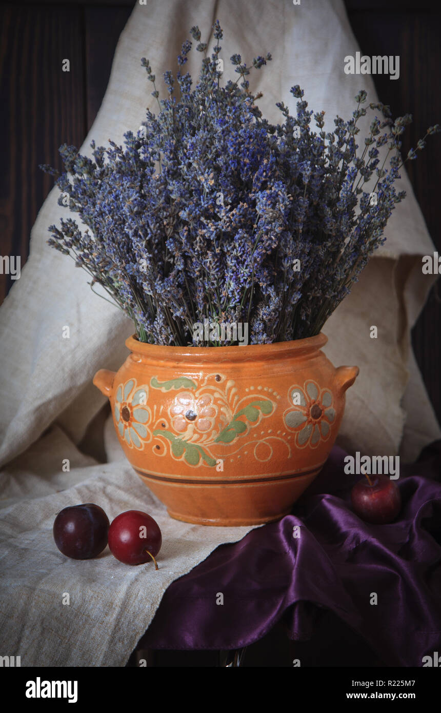 Stillleben mit Lavendel in einem Tonkrug und Pflaumen auf dem Tisch. Country-Stil. Stockfoto