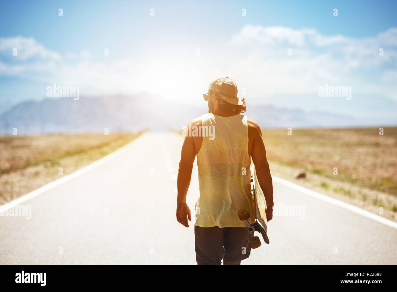 Mann Spaziergänge durch lange gerade Straße oder Autobahn mit Skateboard oder Longboard. Travel Concept Stockfoto