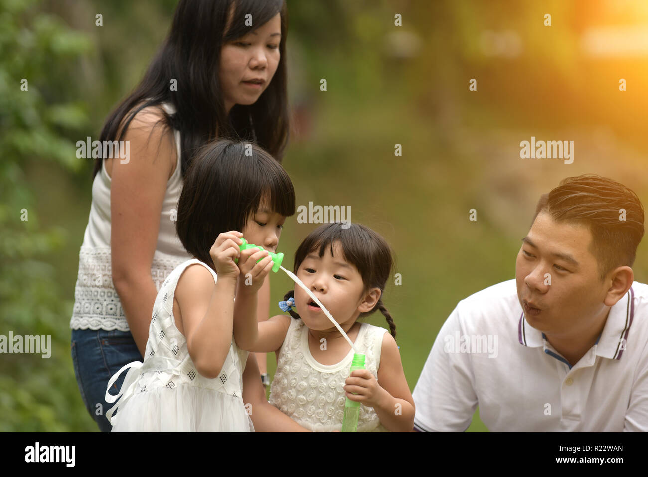 Glückliche junge asiatische Familie spielen mit Bubble Zauberstäbe mit Tochter im Park im Freien Stockfoto