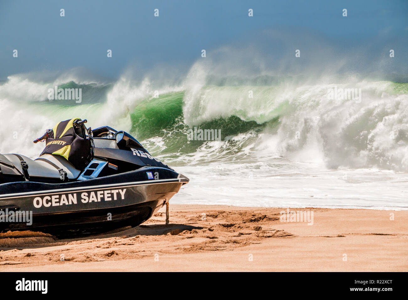 Rettungsschwimmer jetski sitzt auf dem goldenen Sandstrand von Hawaii als Big Wave stürzt im Hintergrund. Stockfoto