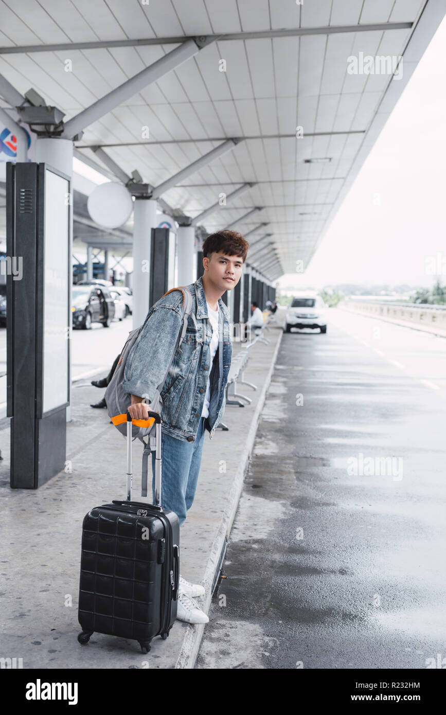 Junger Mann ziehen und Smartphone Koffer in modernen Flughafen Terminal verwenden. Reisen Kerl mit seinem Gepäck während der Wartezeit für den Transport Stockfoto