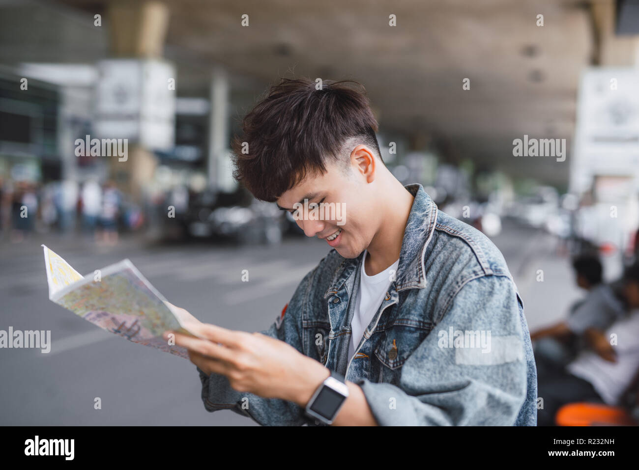 Gut aussehender junger Mann mit Gepäck Tasche auf Stadt Straße mit viel Verkehr Verkehr Suche Karte, Warten auf dem Bus Stockfoto