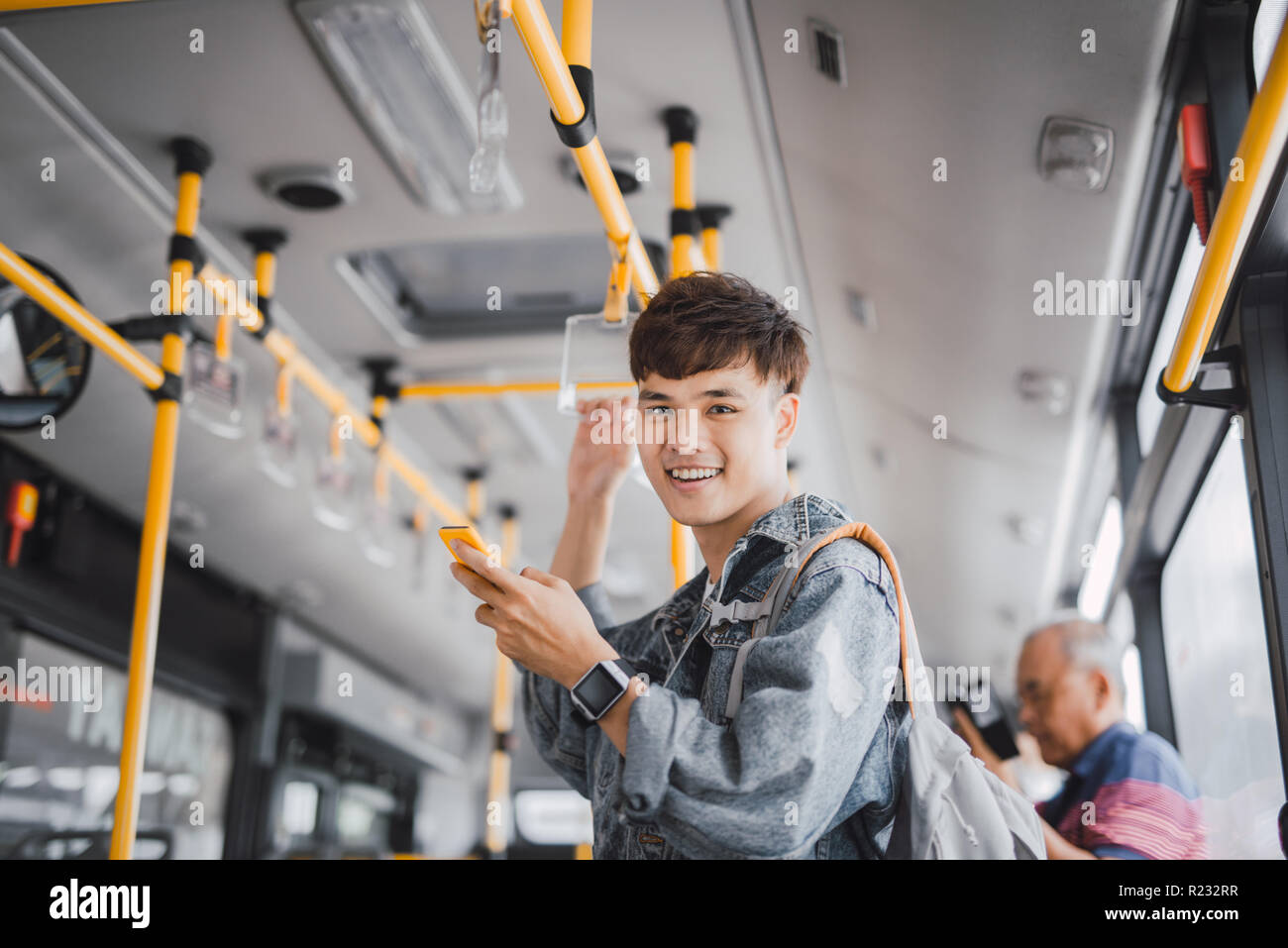 Jungen asiatischen Mann steht im Bus mit Telefon und Festhalten an der Bar, während Sie darauf warten, an ihrem Bestimmungsort ankommen. Stockfoto