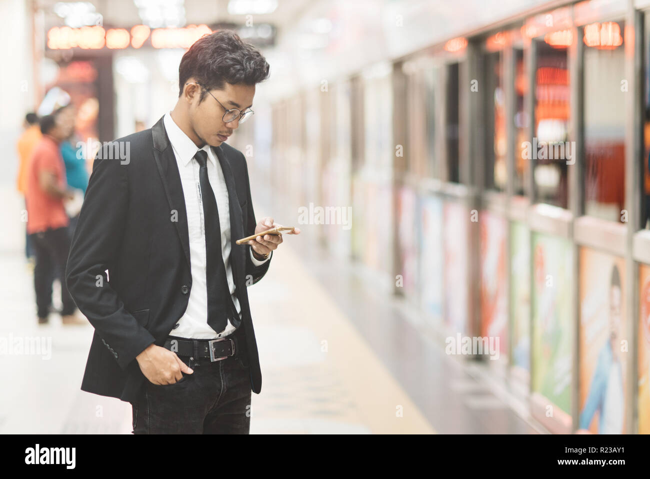 Junge hipster asiatische Geschäftsmann mit Smartphone beim Warten auf einen Zug in der Nähe der U-Bahn. Konzept der drahtlosen Technologie, mobiles Internet und online Busin Stockfoto