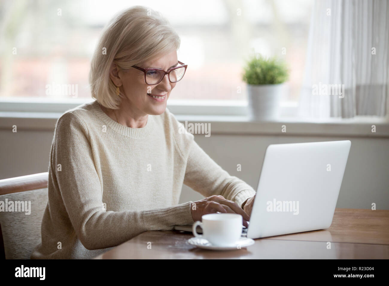 Glücklich im Alter Frau in Gläser am Laptop Tee trinken, lächelnden älteren weiblichen mit Computer suchen oder im Internet surfen, lesen Nachrichten online, ex Stockfoto