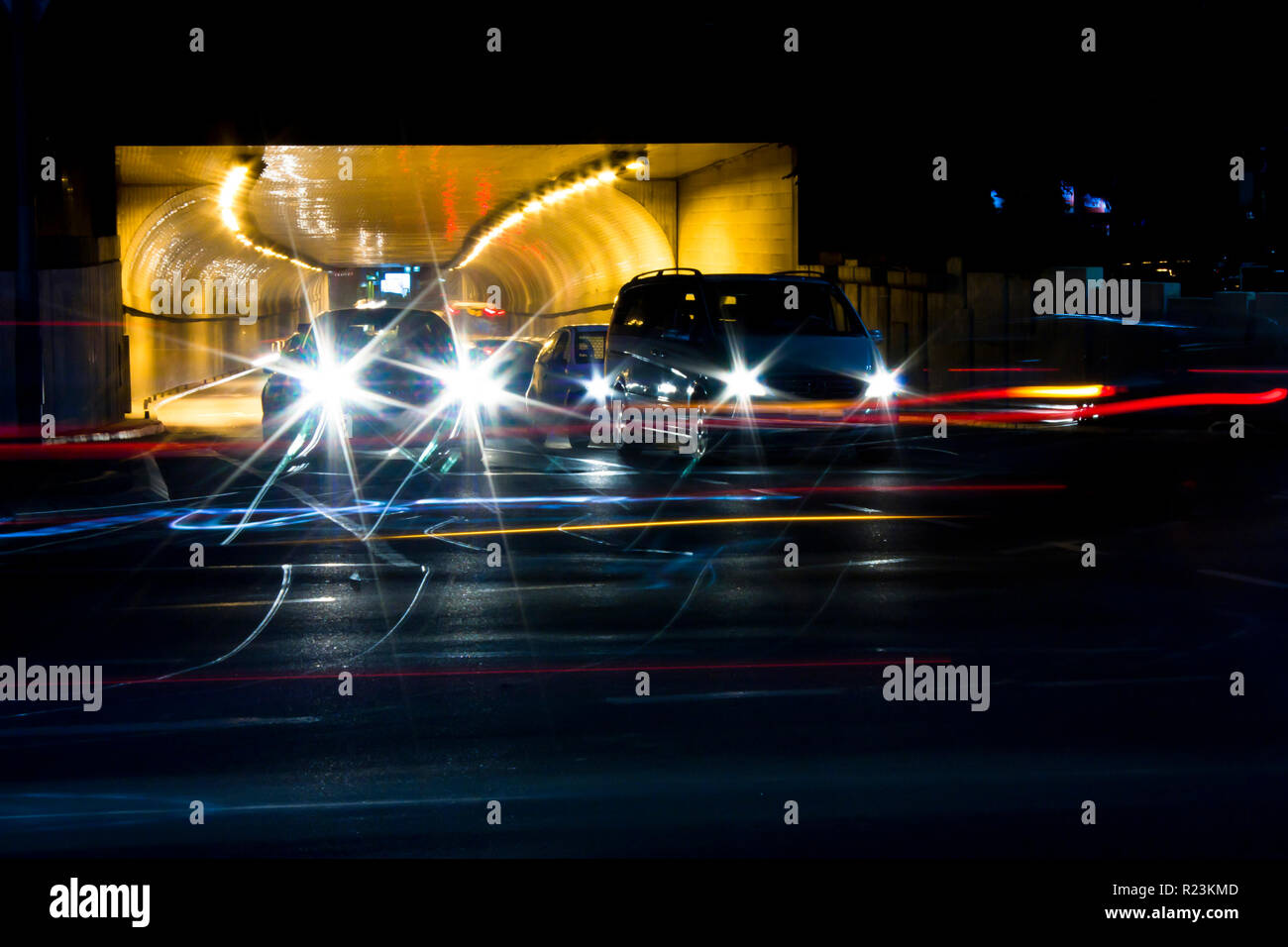 Nachtverkehr auf Straßen der Stadt. Autos in der Warteschlange am Tunnelausgang wartet an Kreuzung beim führen von Fahrzeugen, die bewegte Vergangenheit verlassen Farbe Lichtspuren Stockfoto