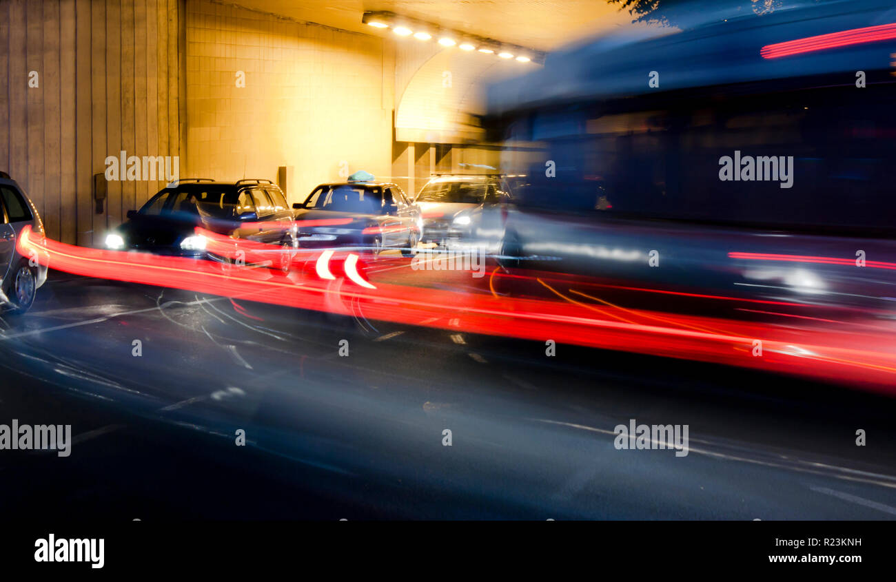 Nachtverkehr auf Straßen der Stadt. Autos in der Warteschlange am Tunnelausgang wartet an Kreuzung beim führen von Fahrzeugen, die bewegte Vergangenheit verlassen Farbe Lichtspuren Stockfoto