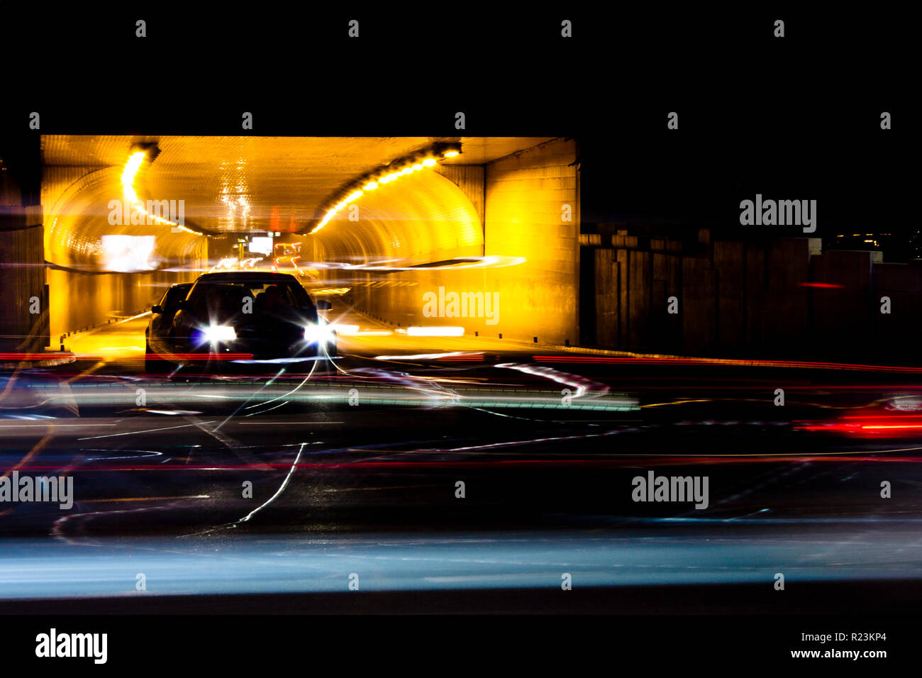 Nachtverkehr auf Straßen der Stadt. Autos in der Warteschlange am Tunnelausgang wartet an Kreuzung beim führen von Fahrzeugen, die bewegte Vergangenheit verlassen Farbe Lichtspuren Stockfoto