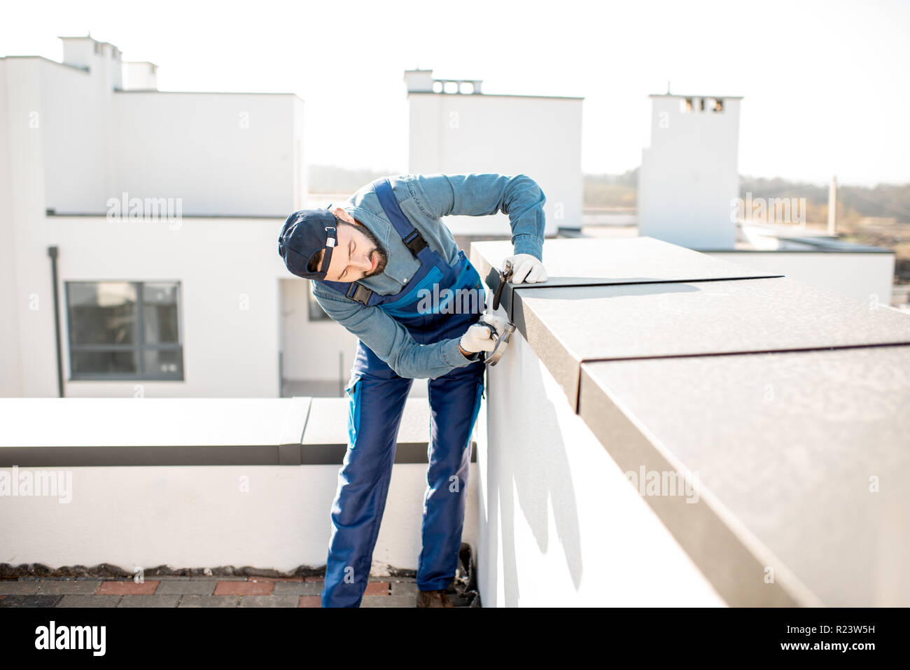 Builder in Uniform die Metallabdeckung an der Brüstung eines neuen Gebäudes Stockfoto