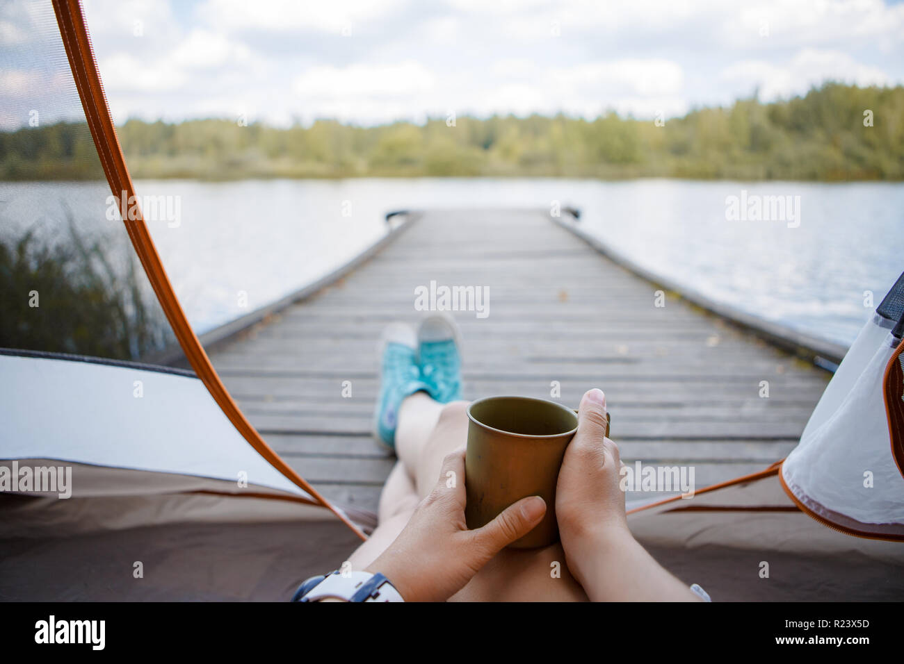 Foto von Frau mit Eisen Becher in die Hände sitzen auf hölzernen Brücke am Fluss Stockfoto