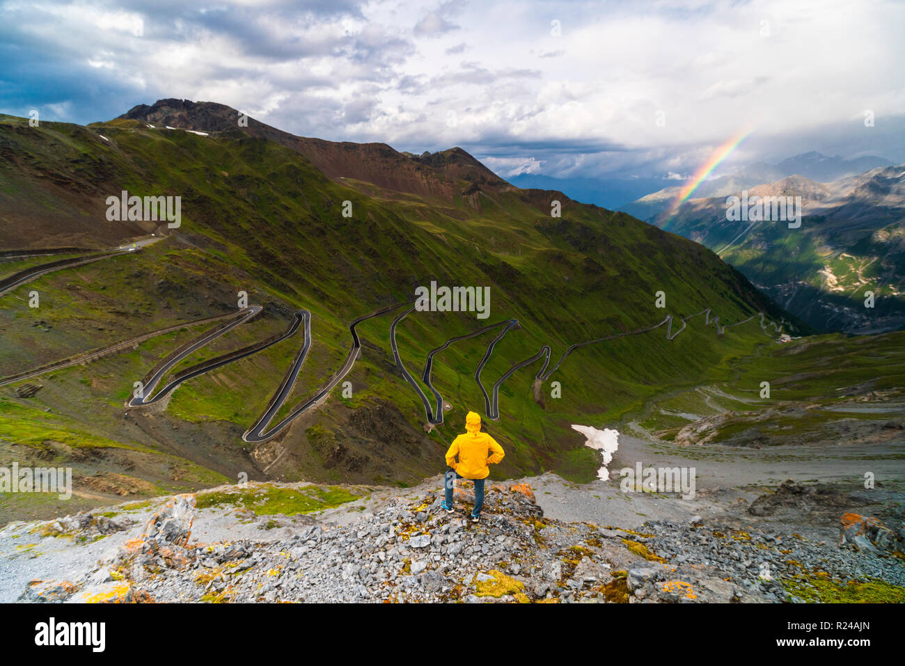 Mann auf Felsen bewundert die Regenbogen auf der kurvenreichen Straße, Stilfser Joch, Südtirol Seite, Valtellina, Lombardei, Italien, Europa Stockfoto