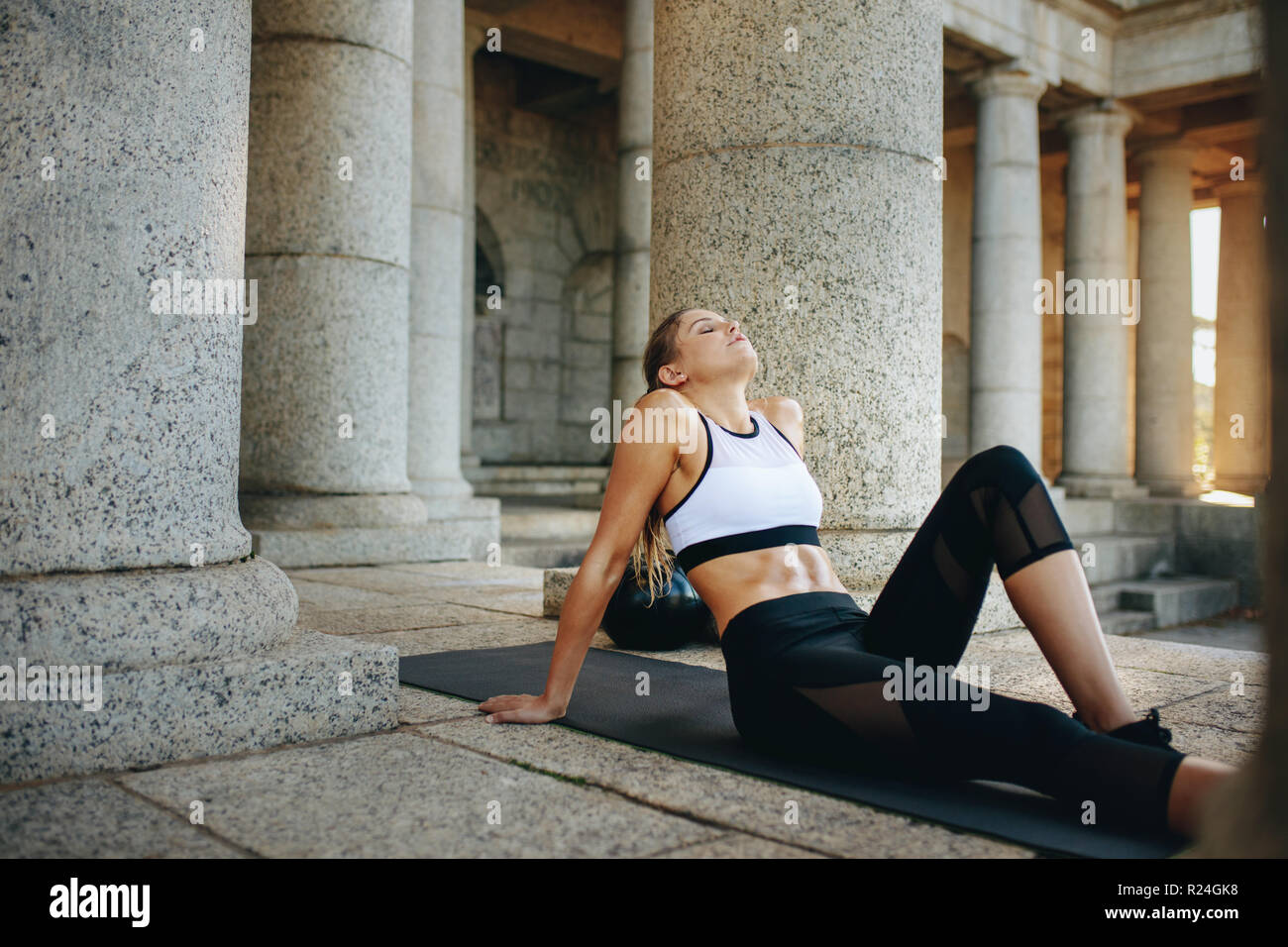 Fitness-Frau, die sich nach dem Training mit geschlossenen Augen auf einer Trainingsmatte entspannt. Weibliche Athletin, die Fitnesstraining macht, sitzt auf Yogamatte mit einem Medikament bal Stockfoto