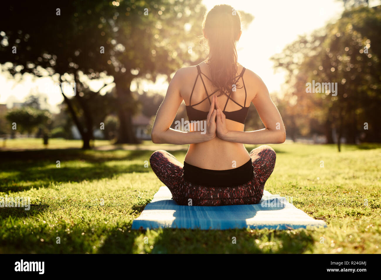Frau macht Yoga im Park, umgekehrte Gebetsposition. Fitness-Frau, die Pashchima Namaskarasana Yoga macht, sitzt auf Matte im Park. Rückansicht von fema Stockfoto