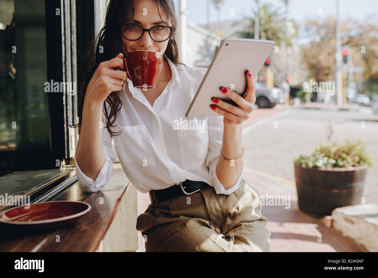 Frau, die eine Brille im Café trägt, mit einem digitalen Tablet, das Kaffee trinkt. Geschäftsfrau trinkt Kaffee im Café. Stockfoto
