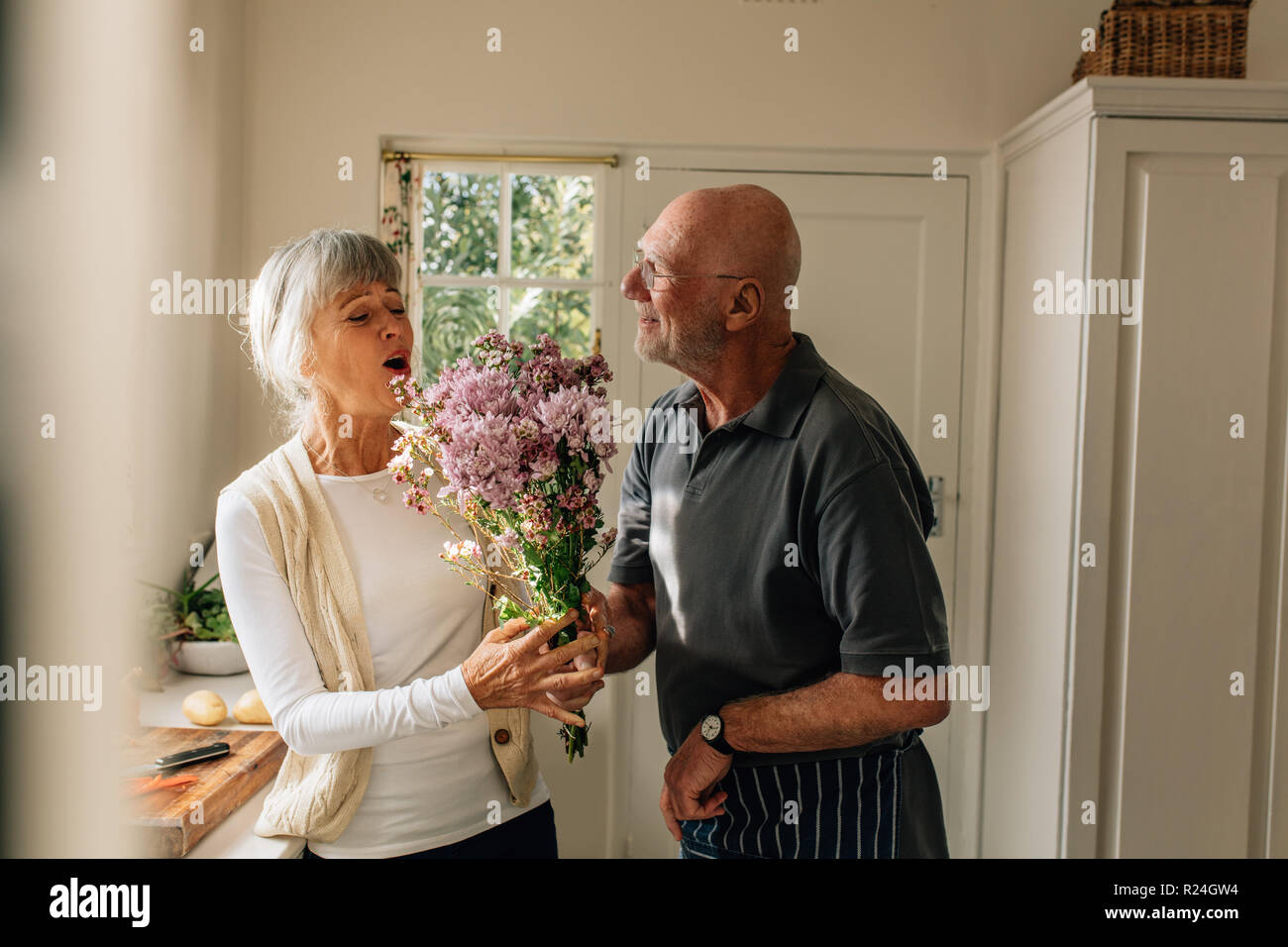 Der Mensch seine Liebe für seine Frau, die ihr ein paar Blumen zu Hause zum Ausdruck zu bringen. Ältere Frau glücklich zu sehen, ihr Mann ihr einen Strauß Blumen zu schenken. Stockfoto