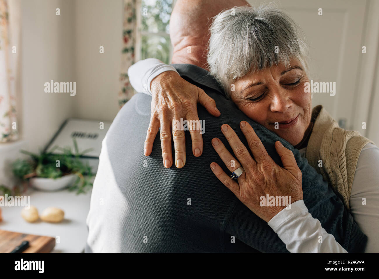 Nahaufnahme von einer älteren Frau, die ihren Ehemann mit geschlossenen Augen stehen in der Küche. Ältere Paare umarmen Ausdruck ihrer tiefen Liebe ein Stockfoto